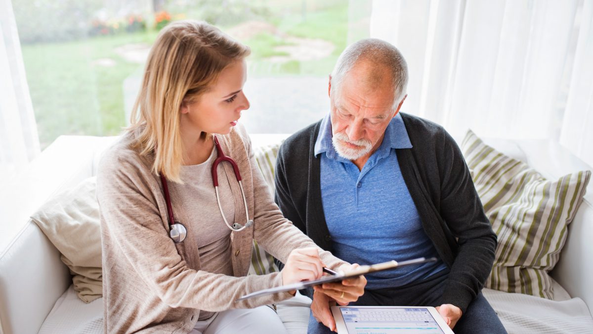 Health visitor and a senior man with tablet during home visit.