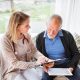 Health visitor and a senior man with tablet during home visit.