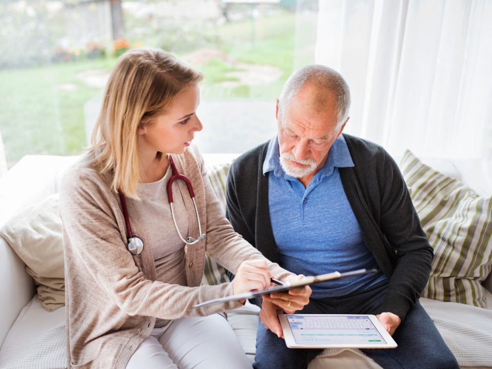 Health visitor and a senior man with tablet during home visit.