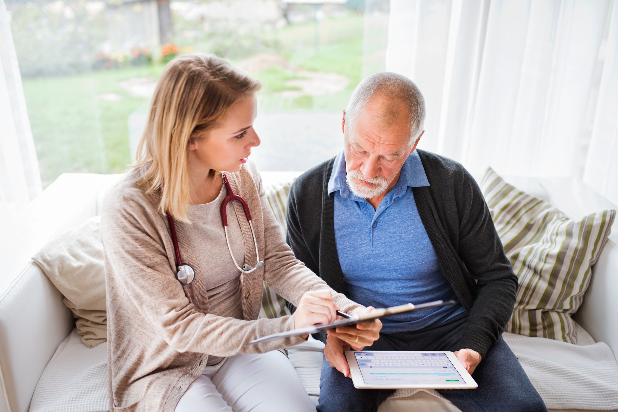 Health visitor and a senior man with tablet during home visit.